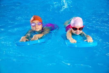two little girls having fun in pool learning how to swim using flutterboards
